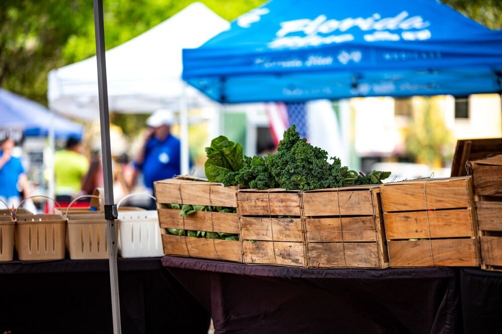 Wooden crates of fresh greens at an outdoor farmers market under a Florida-branded tent