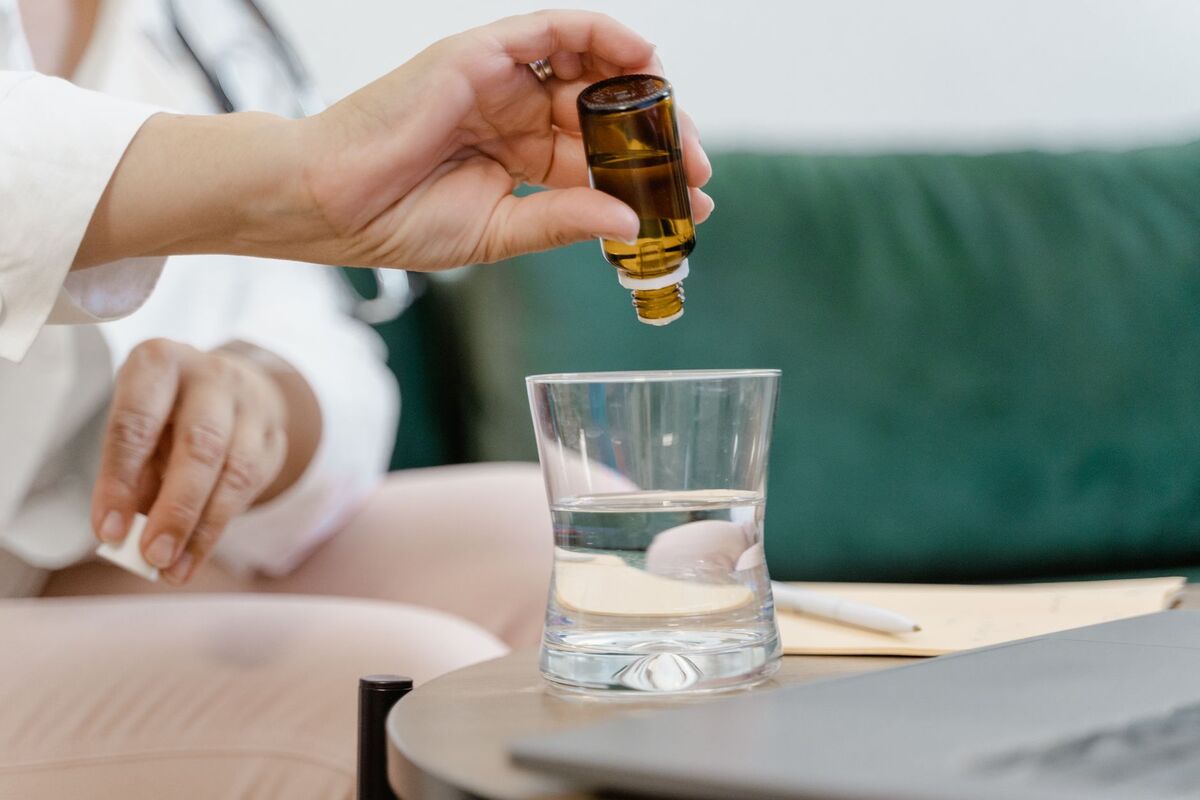 Hands adding drops from an amber tincture bottle into a glass of water