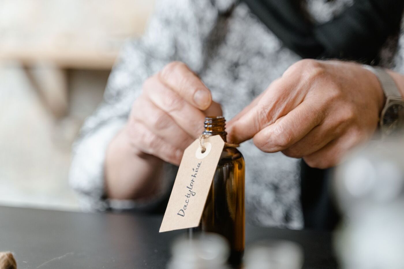 Hands tying a handwritten kraft paper tag onto a small amber bottle