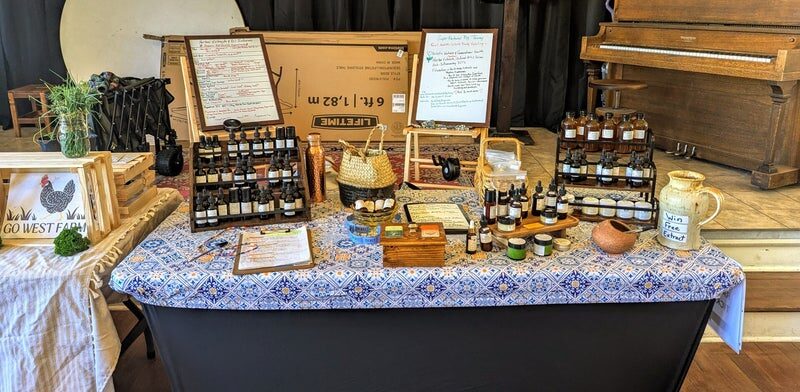 RedFern's farmers market booth with racks of extract bottles, handwritten boards, and a patterned tablecloth